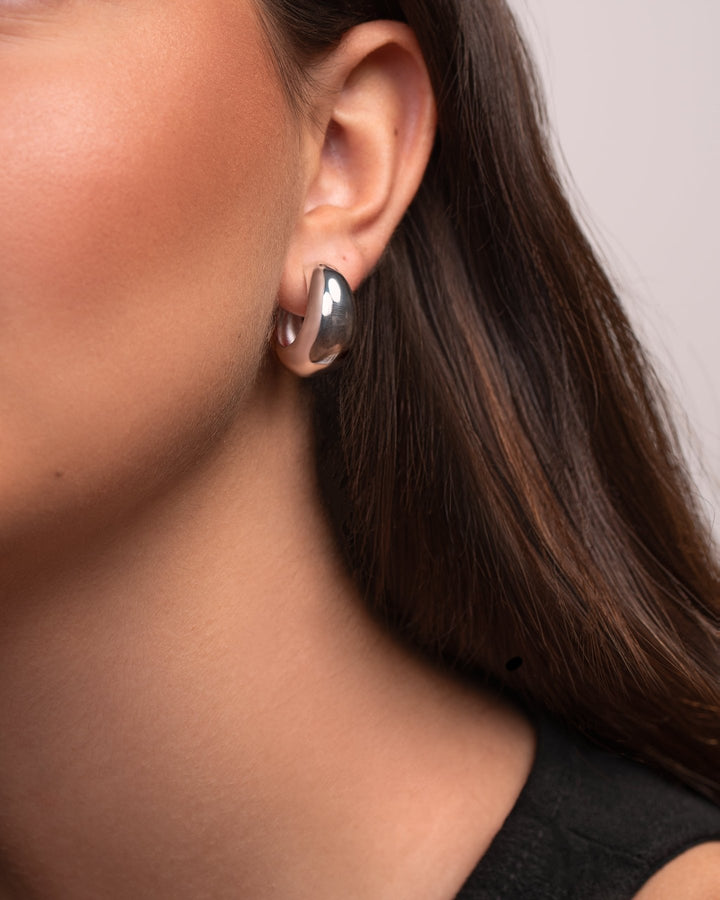 Close-up of a person wearing a silver hoop earring with a neutral background