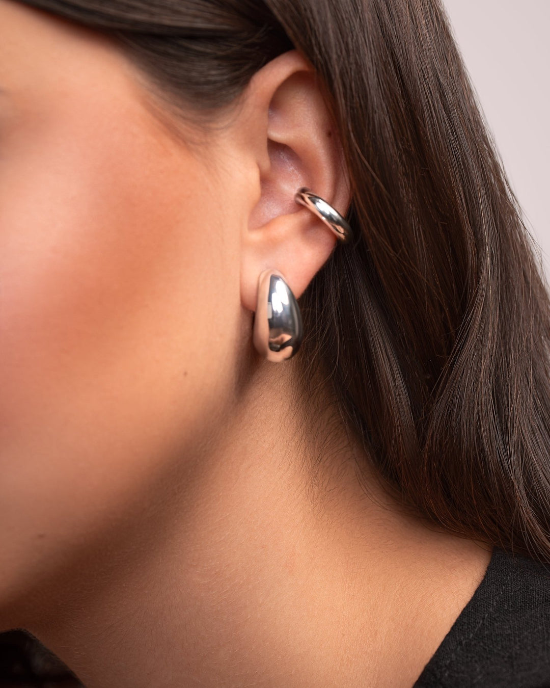 Close-up of a person wearing two rose gold hoop earrings.