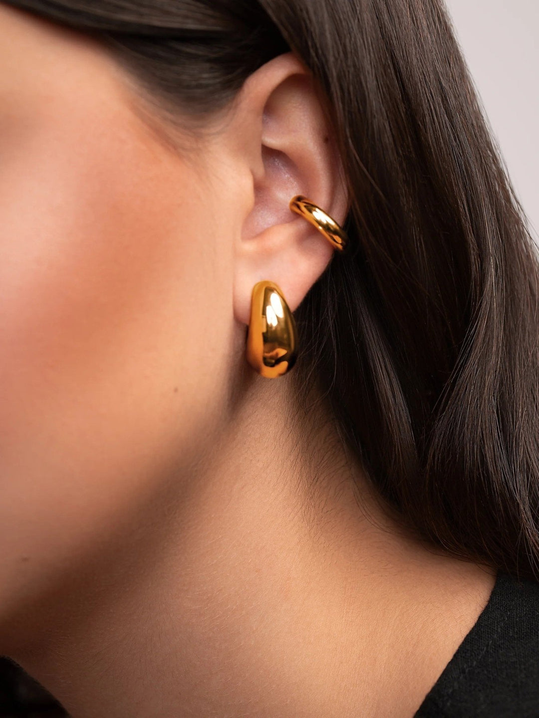 Close-up of a person wearing gold hoop earrings with a neutral background