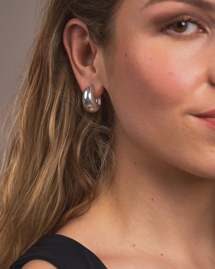 Close-up of a woman wearing a silver hoop earring against a neutral background