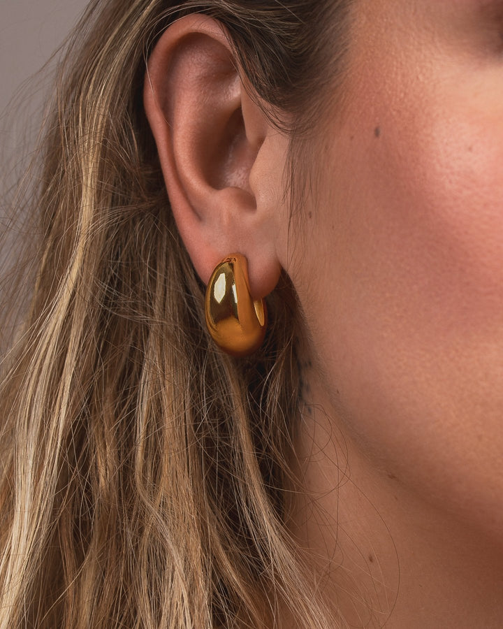 Close-up of an ear wearing a gold hoop earring with a blurred background