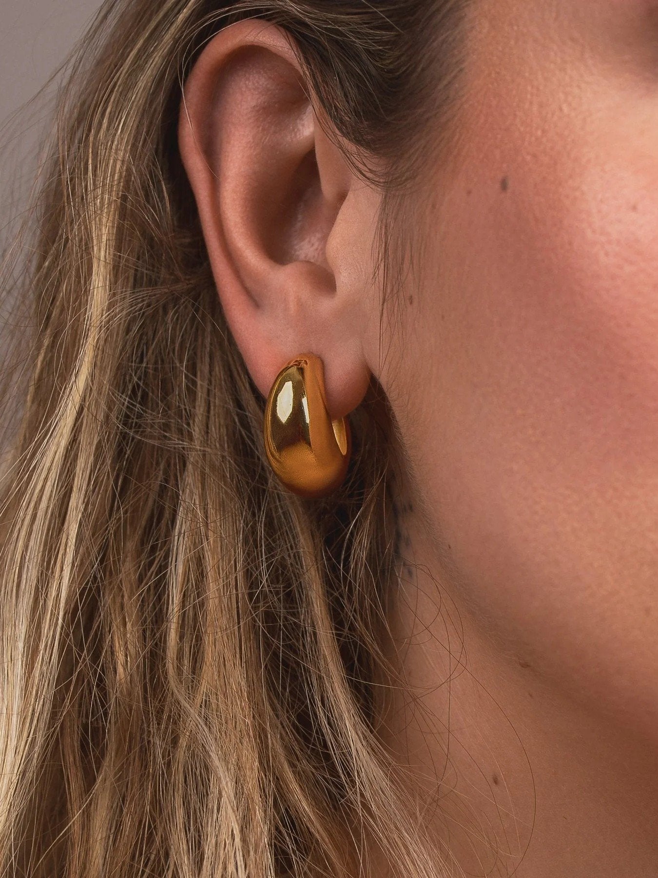 Close-up of an ear wearing a gold hoop earring with a blurred background