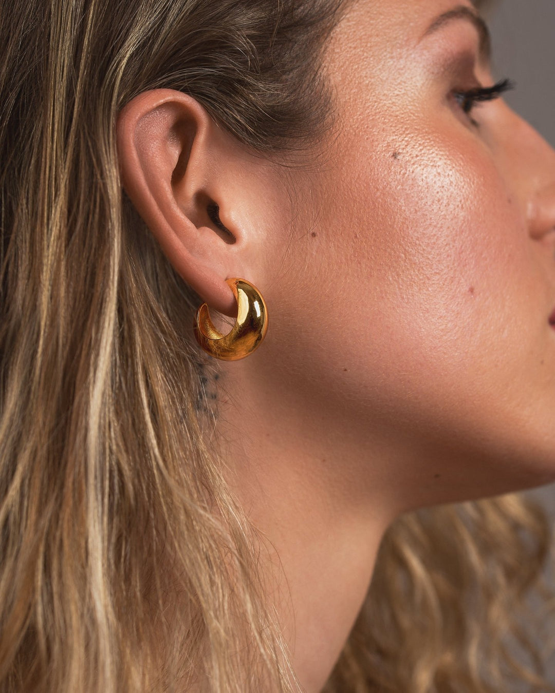Close-up of a woman wearing a gold hoop earring with a neutral background
