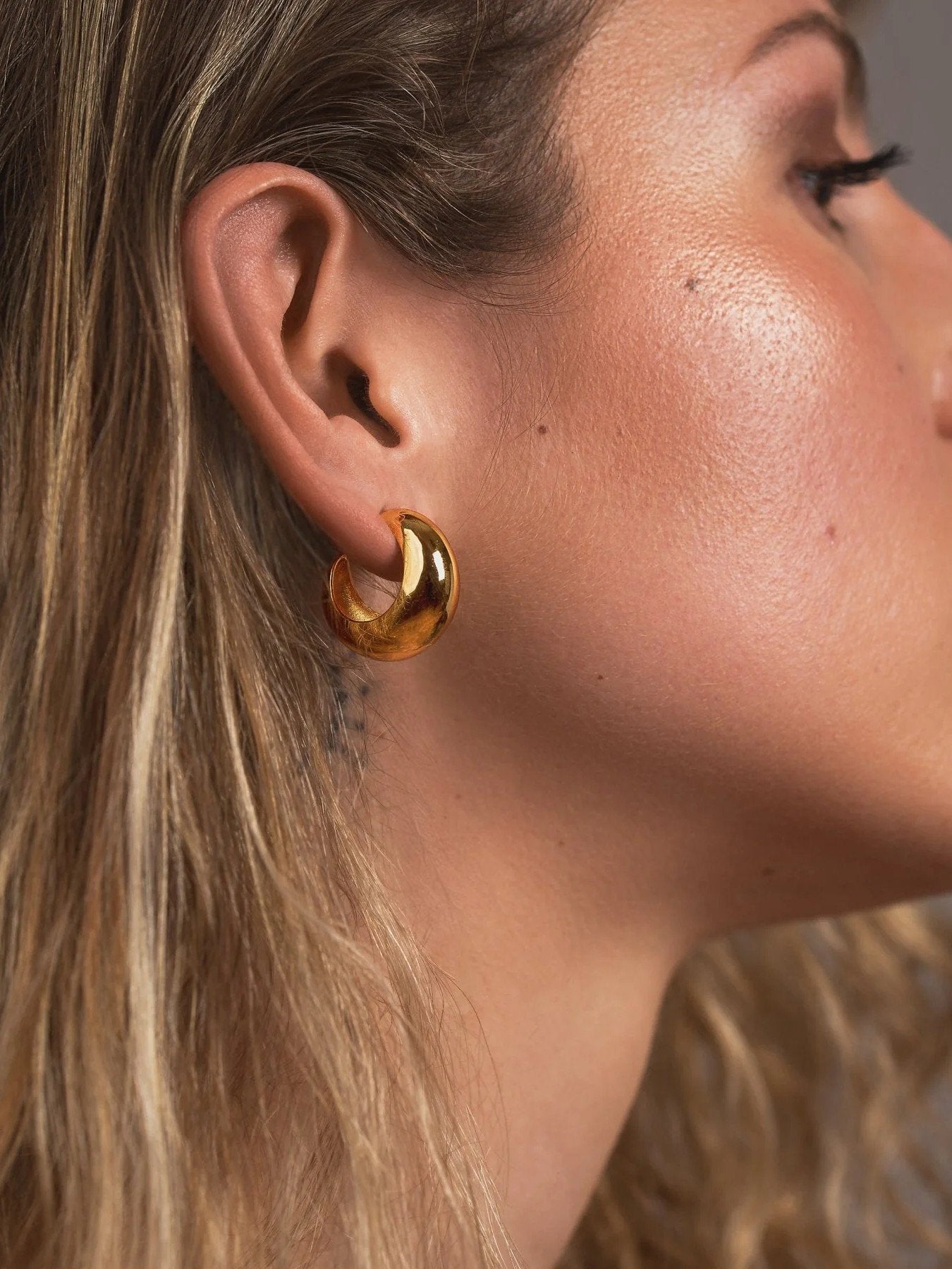 Close-up of a woman wearing a gold hoop earring with a neutral background