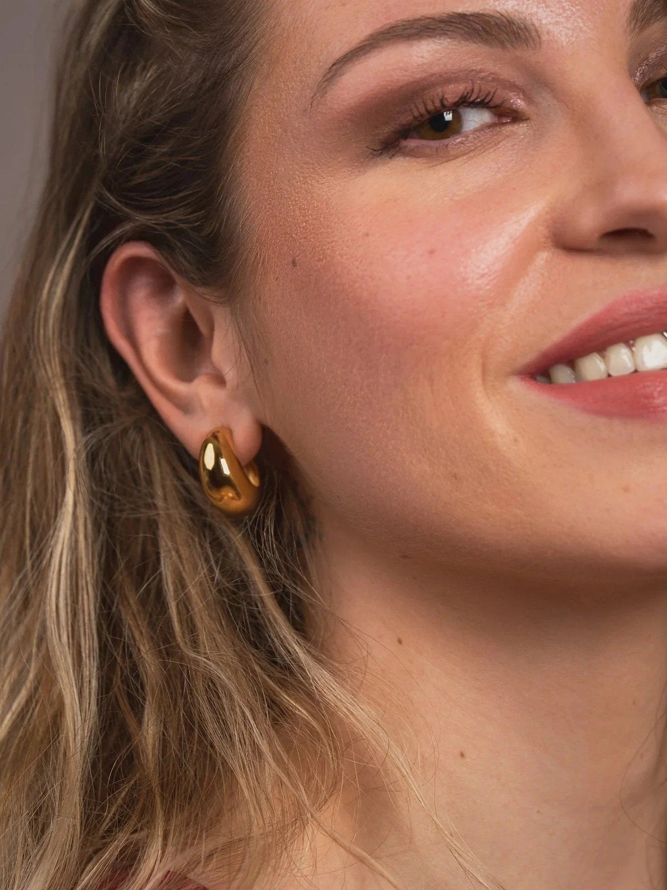 Close-up of a woman wearing gold earrings with a neutral background
