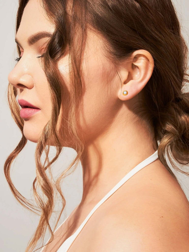 Close-up of model wearing gold stud earrings with natural gemstones.