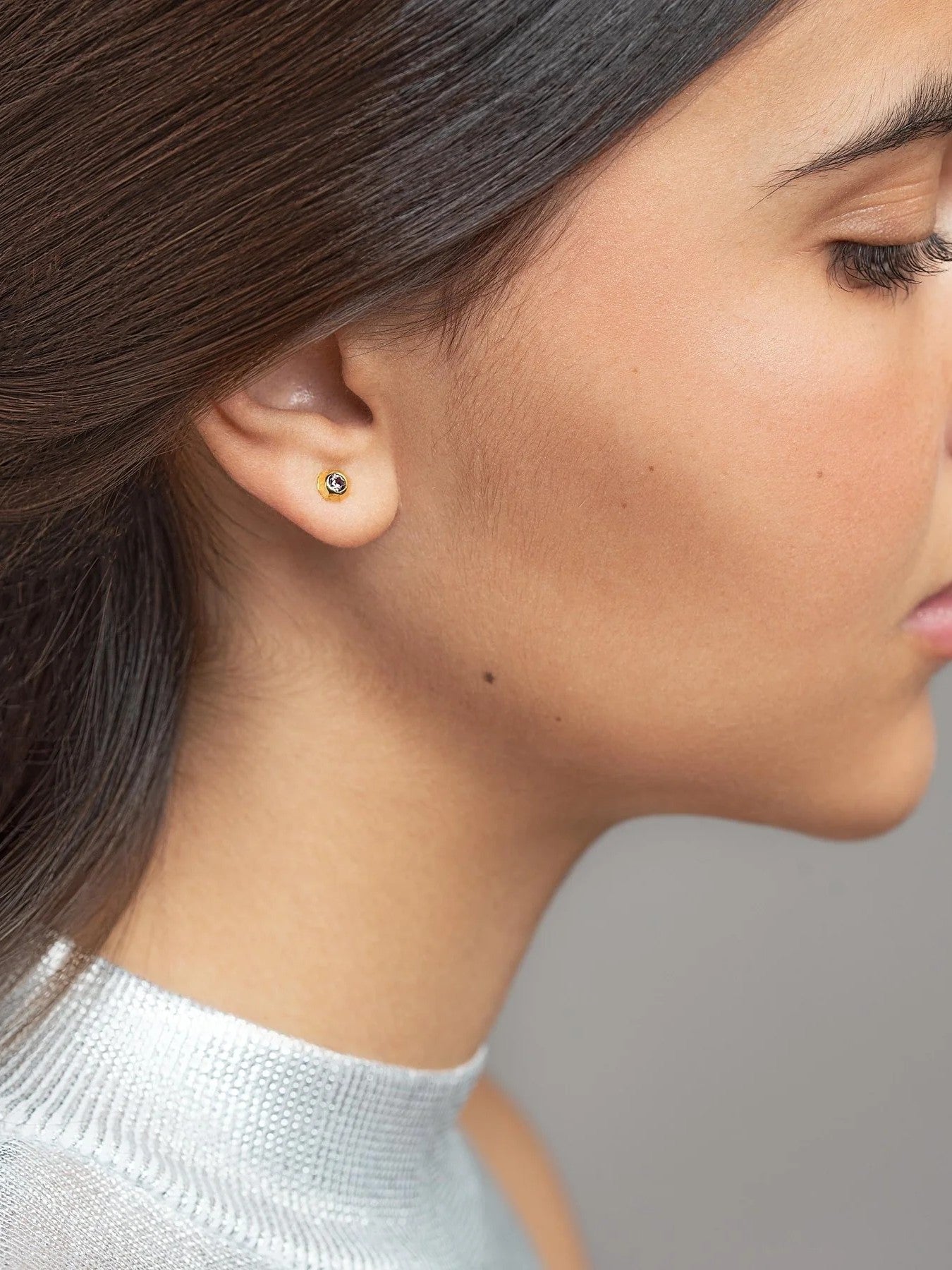 Profile view of a woman wearing a small gold stud earring against a neutral background.