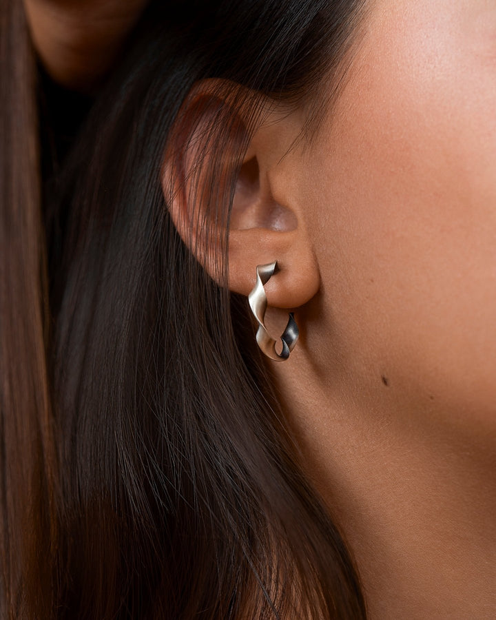 "Model wearing Gene Twisted Hoop Earrings in silver oxide, side view"