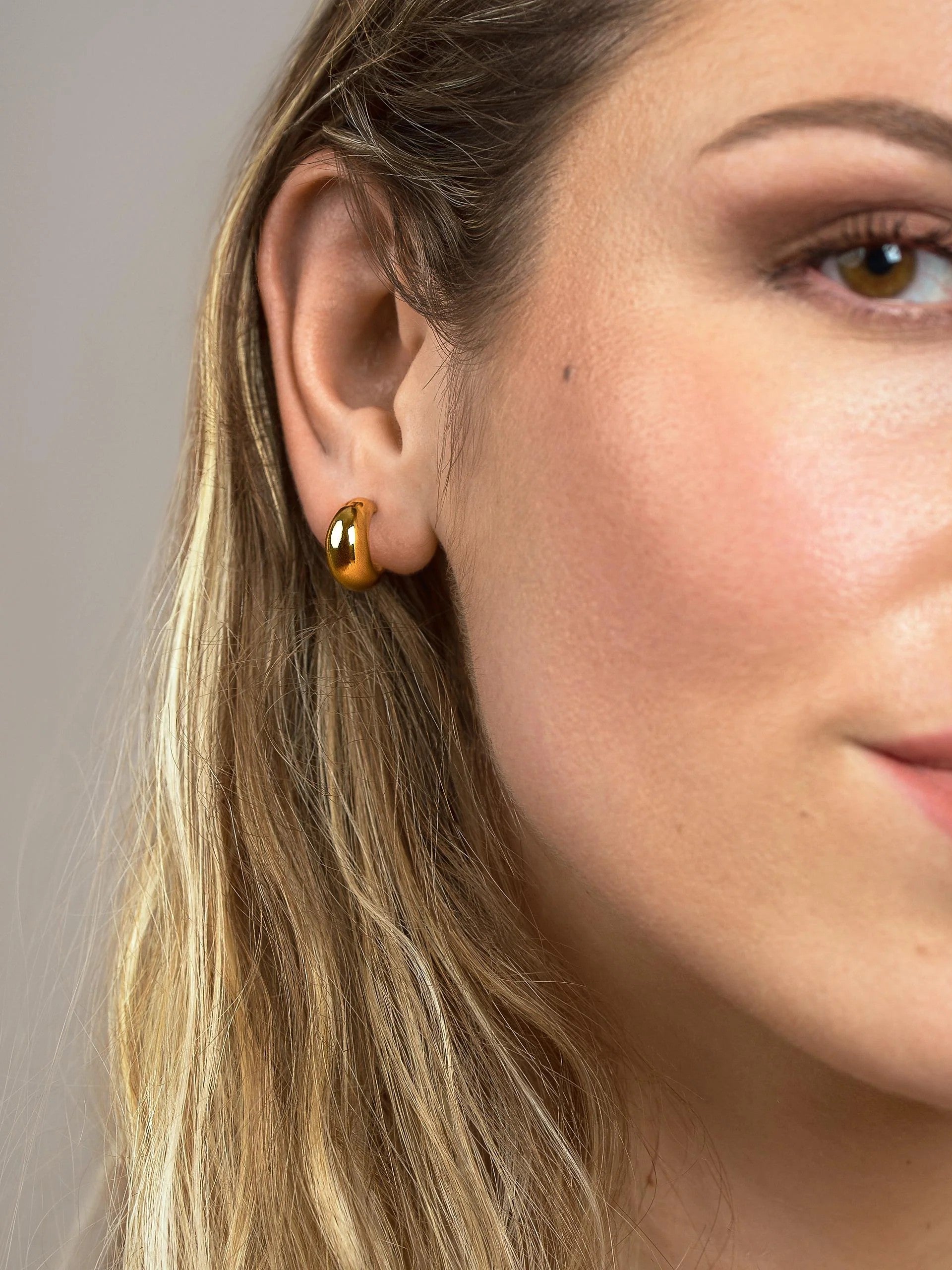 Model wearing small gold plated crescent hoop earrings, front side view showing their petite proportions.