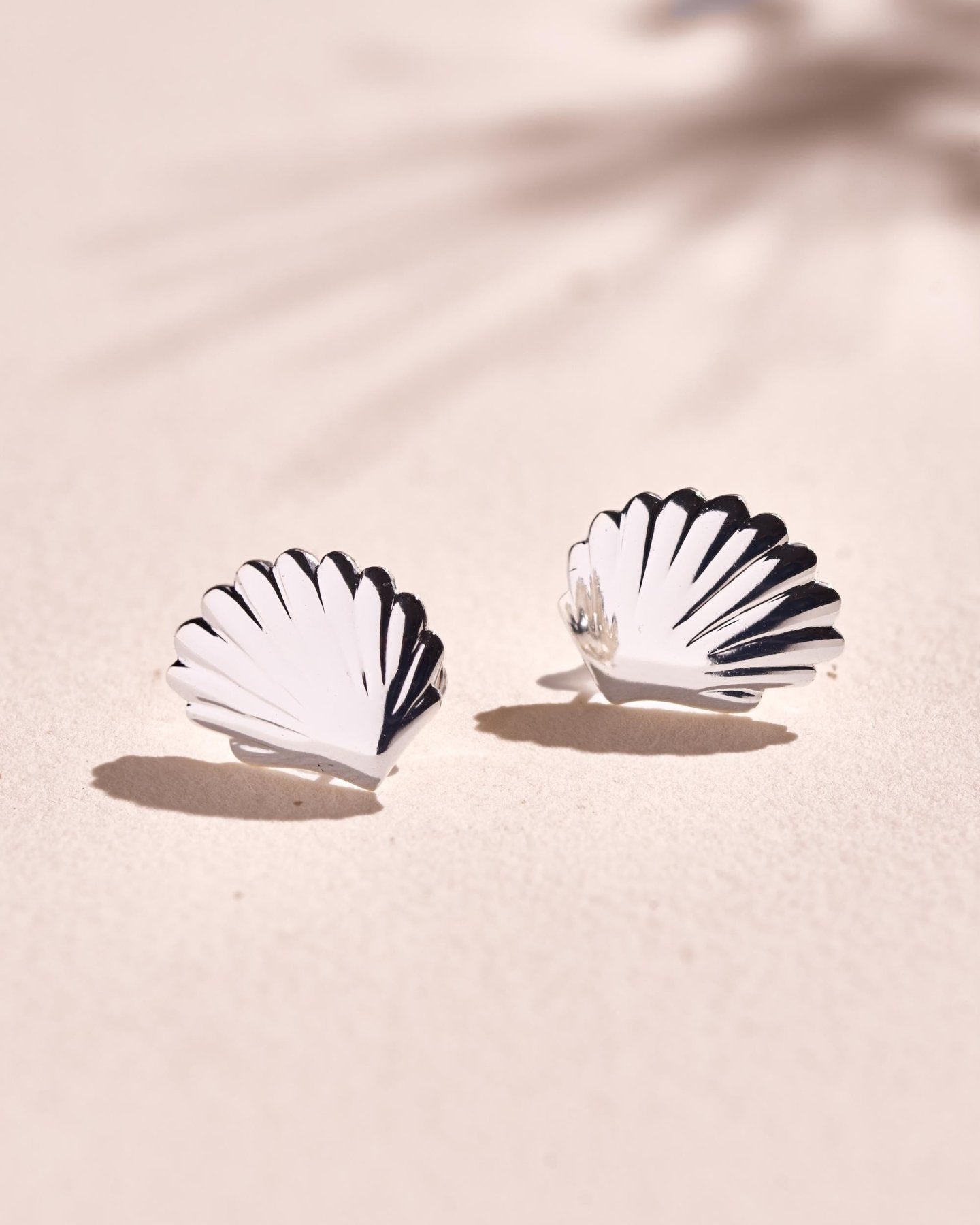 Pair of polished silver shell stud earrings shown from the front with a sculptural scallop design.