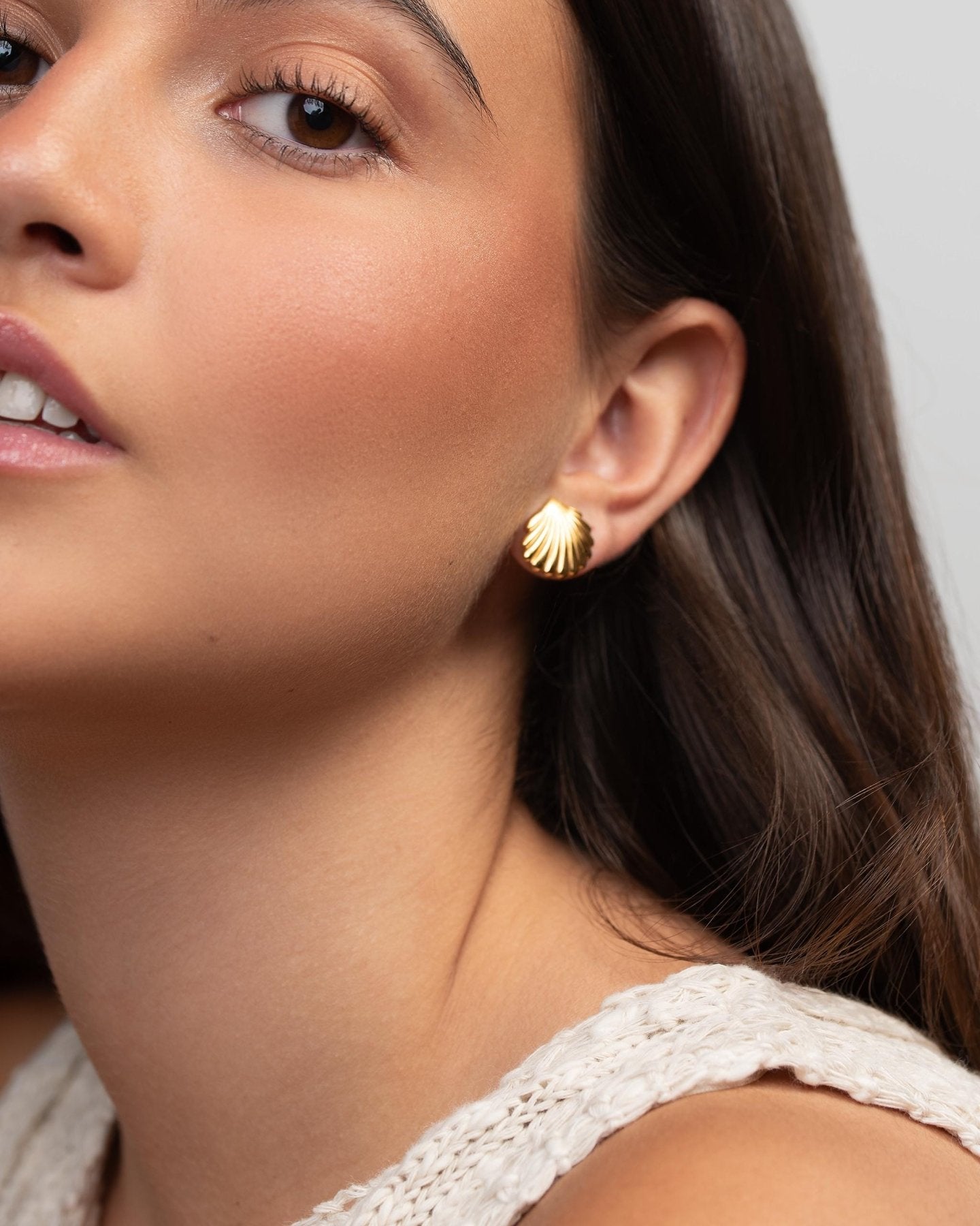 Model wearing a gold shell stud earring, showing the small statement shape and scale on the earlobe.