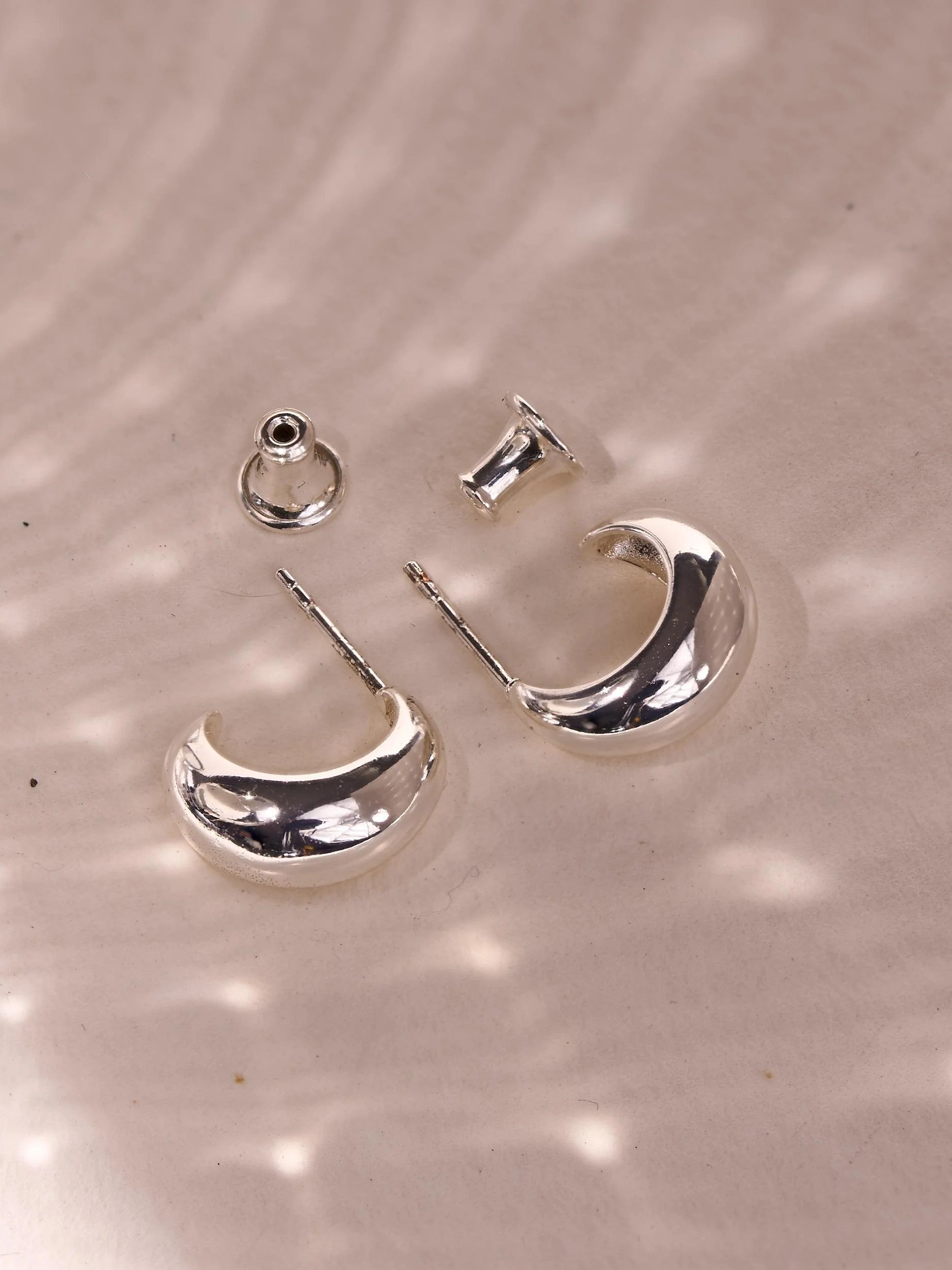 Close-up of petite silver plated crescent hoops showing their smooth polished surface and rounded shape.
