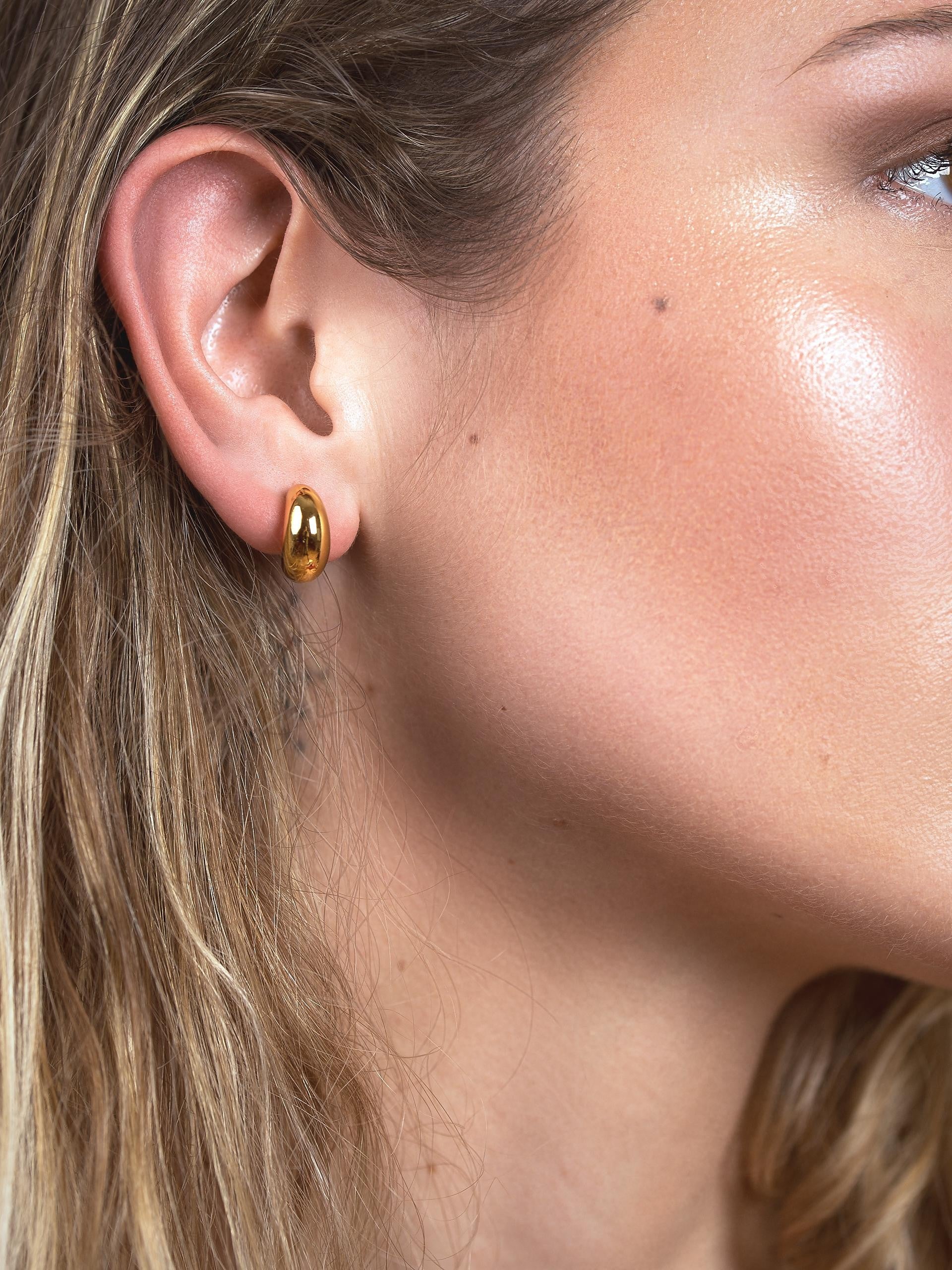 Model wearing petite gold crescent hoop earrings, showing their small scale and close fit on the earlobe.