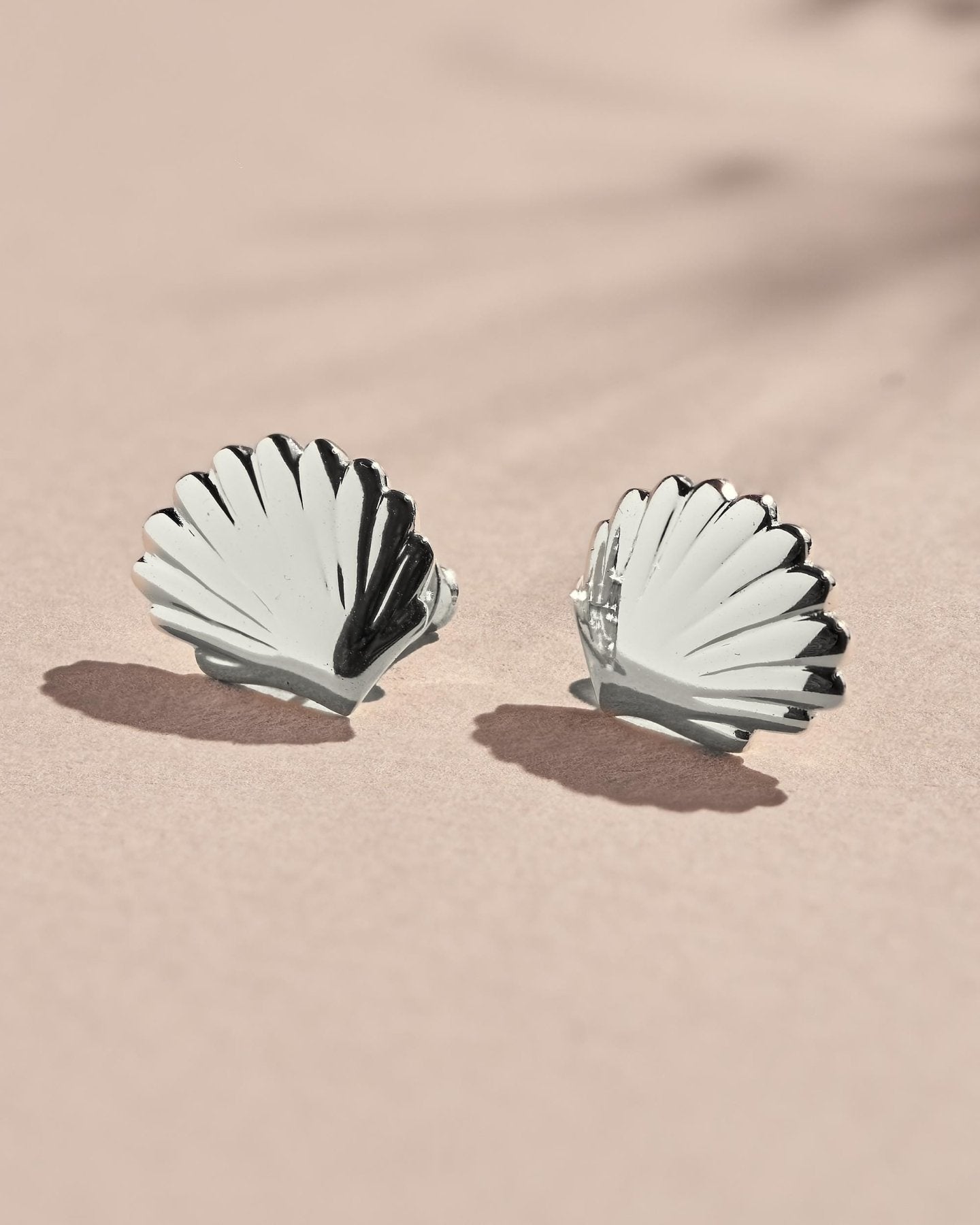 Silver seashell stud earrings photographed as a pair with a bright polished finish and fluted details.
