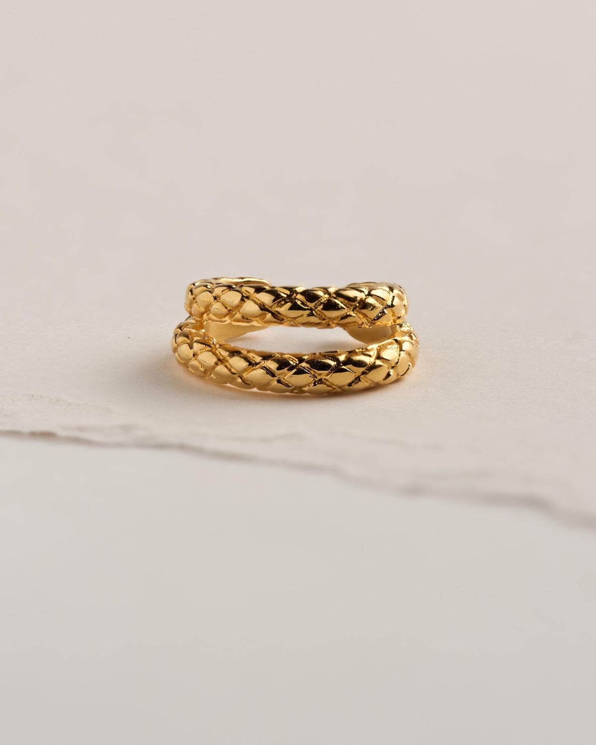 24k gold plated brass snake ear cuff with two textured bands of engraved snake scales, shown from the front on cream torn paper.