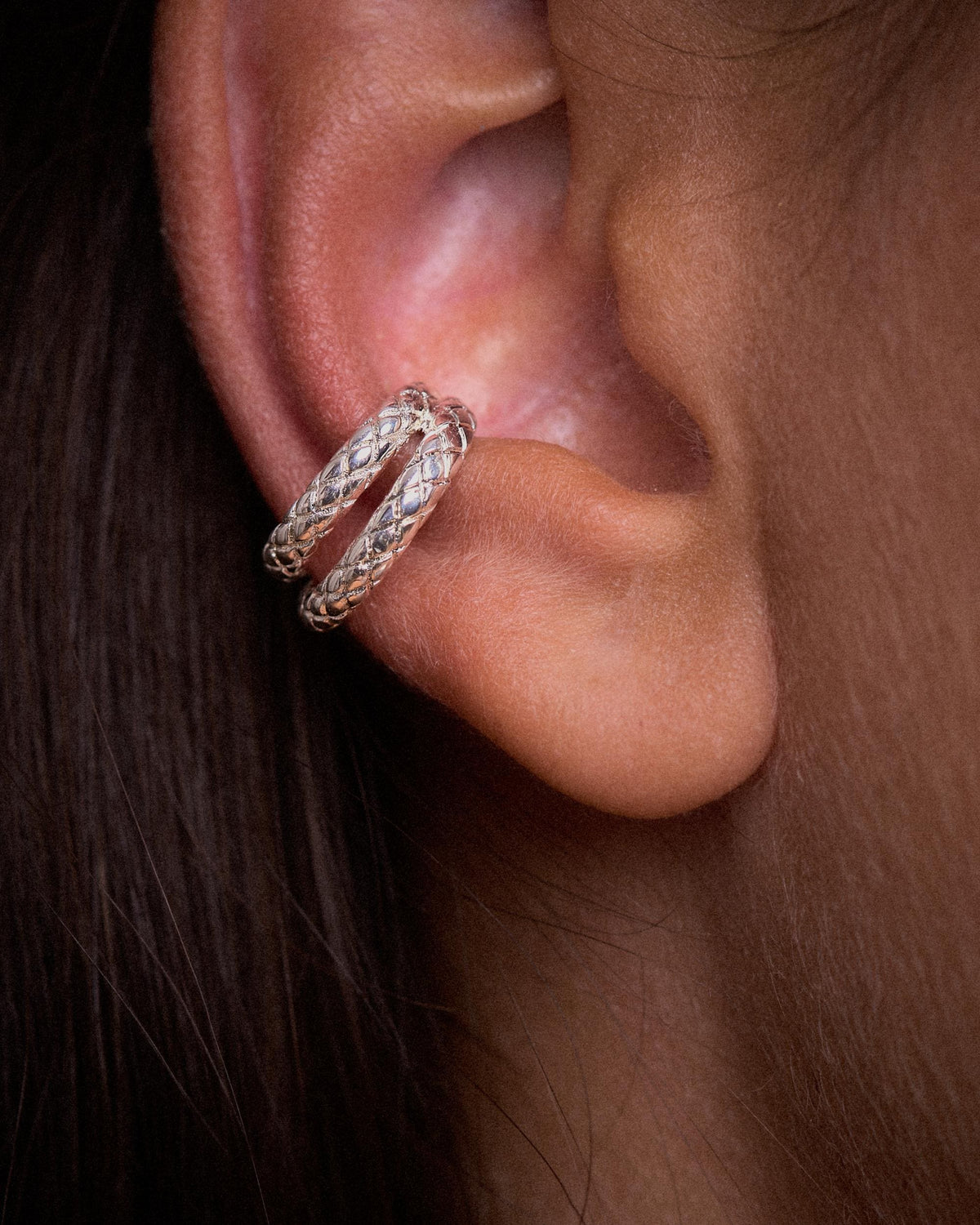 Close-up of an ear wearing a sterling silver plated brass snake ear cuff on the conch, with two bands of engraved snake-scale texture.