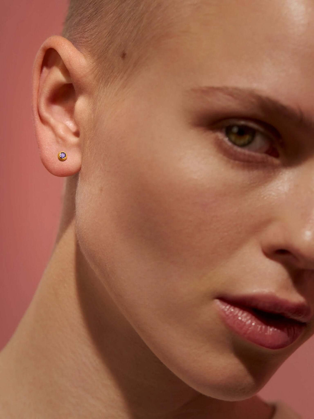 Close-up of model with shaved head wearing gold gemstone stud earrings.