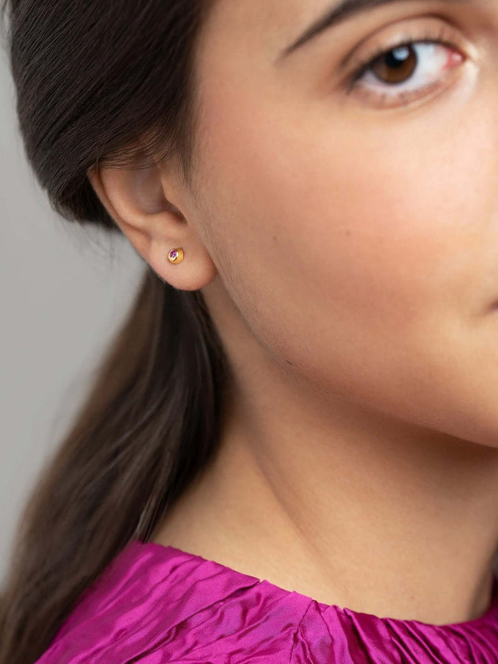 Model wearing a single gold stud earring with a dainty gemstone.