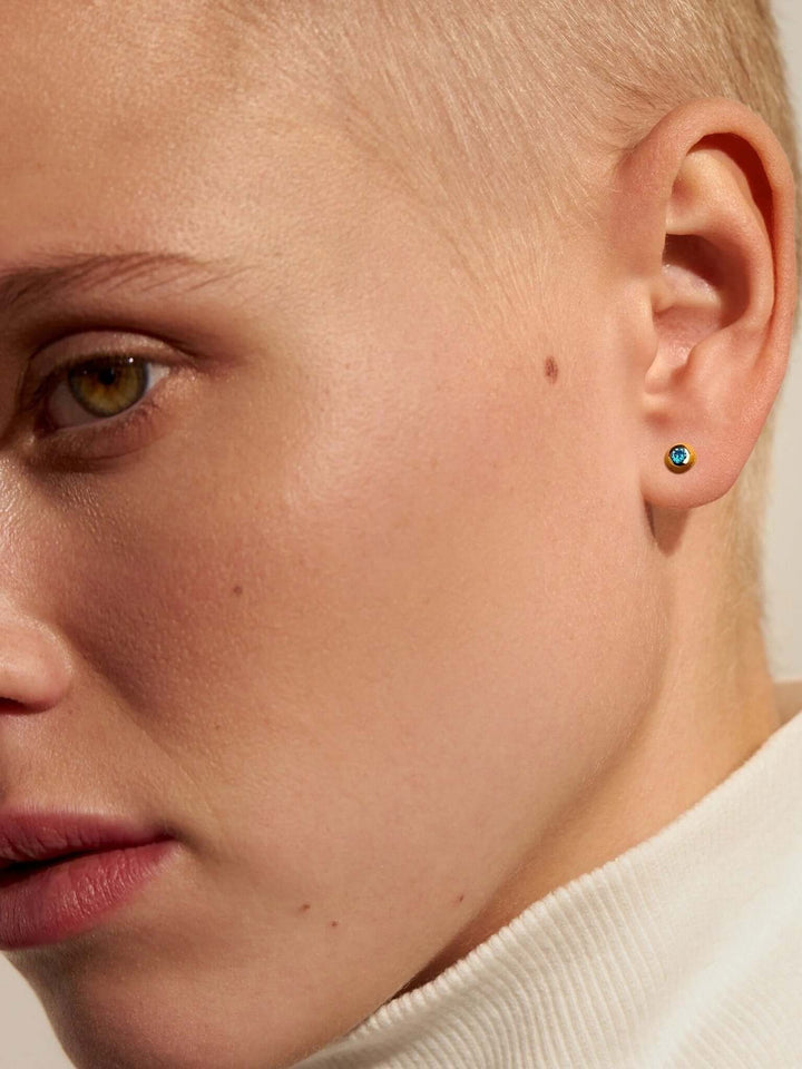 Side profile of model wearing small gold gemstone earrings.