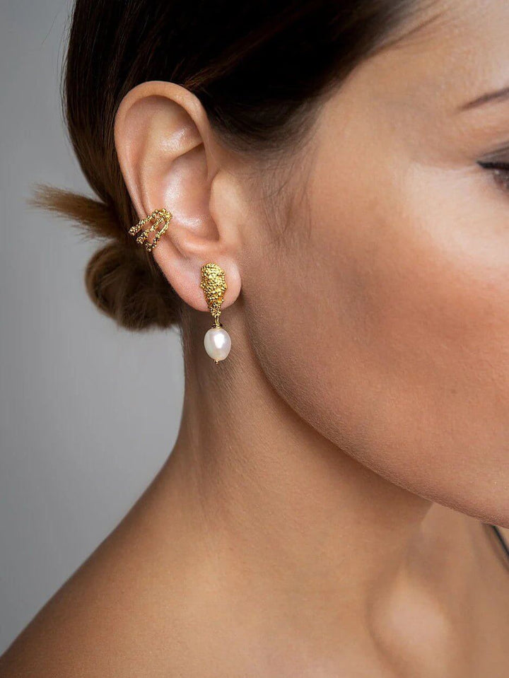 Model in profile wearing baroque pearl earrings, textured stud and natural pearl visible.