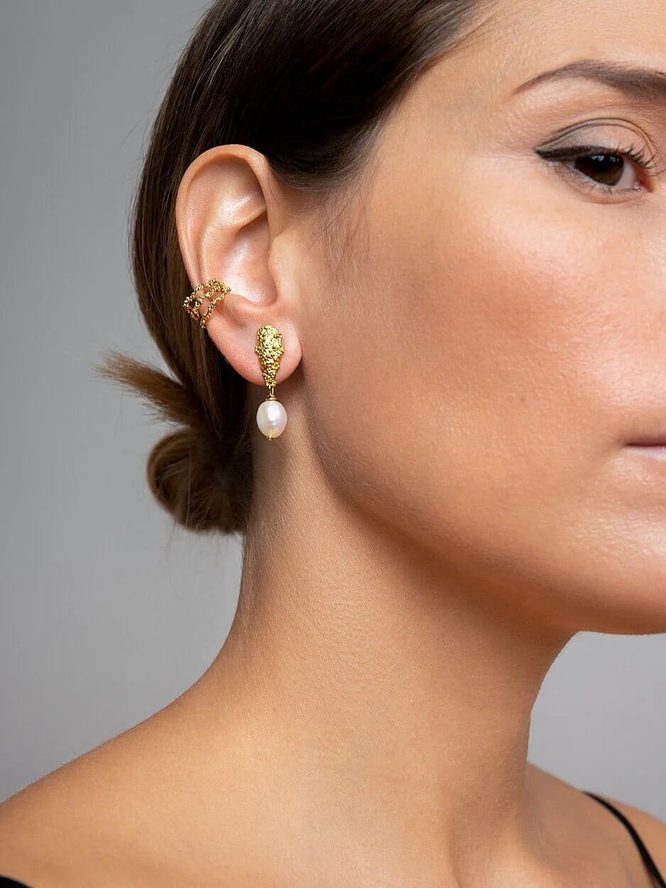 Side view of model with pearl earrings, clean background and elegant pose.