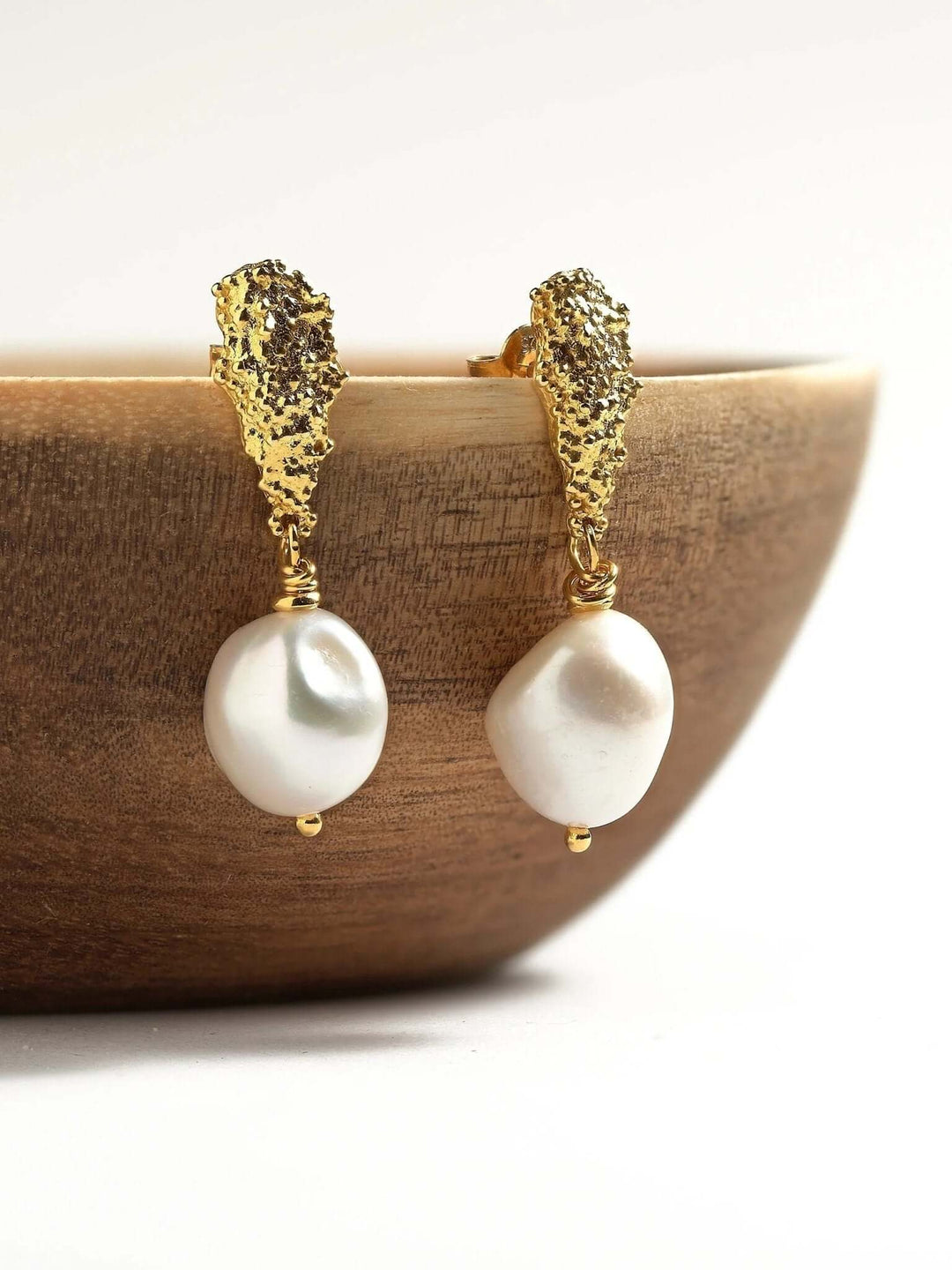 Baroque pearl earrings with organic textured gold studs, displayed on wooden bowl.