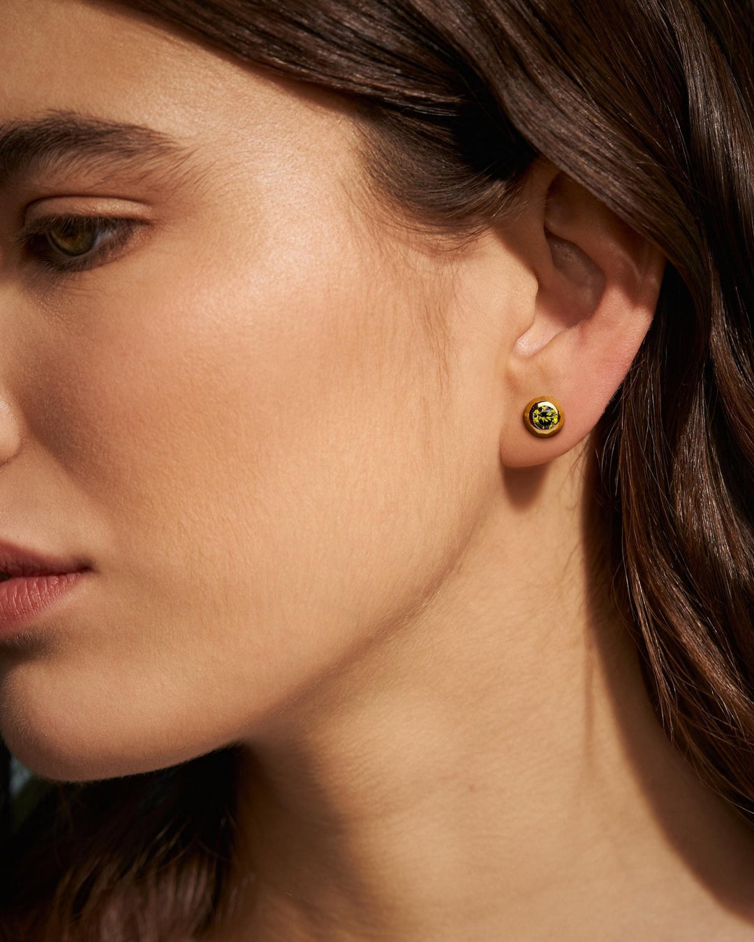 Woman wearing gold earrings with a green stone, side profile – model in profile highlighting the glow of the pink gemstone earring.
