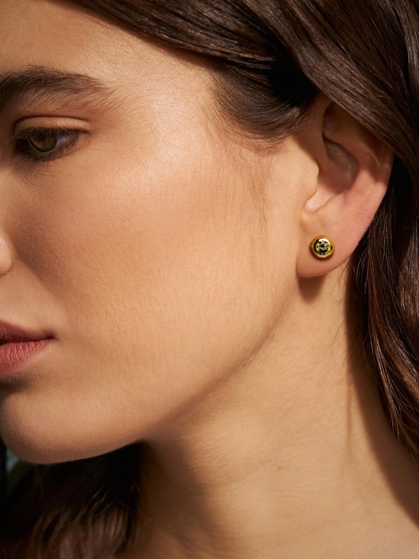 Woman wearing gold earrings with a green stone, side profile – model in profile highlighting the glow of the pink gemstone earring.