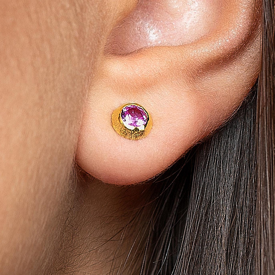 Close-up of pink stone earring on ear – gold stud earring with a pink gemstone, detailed view on skin.