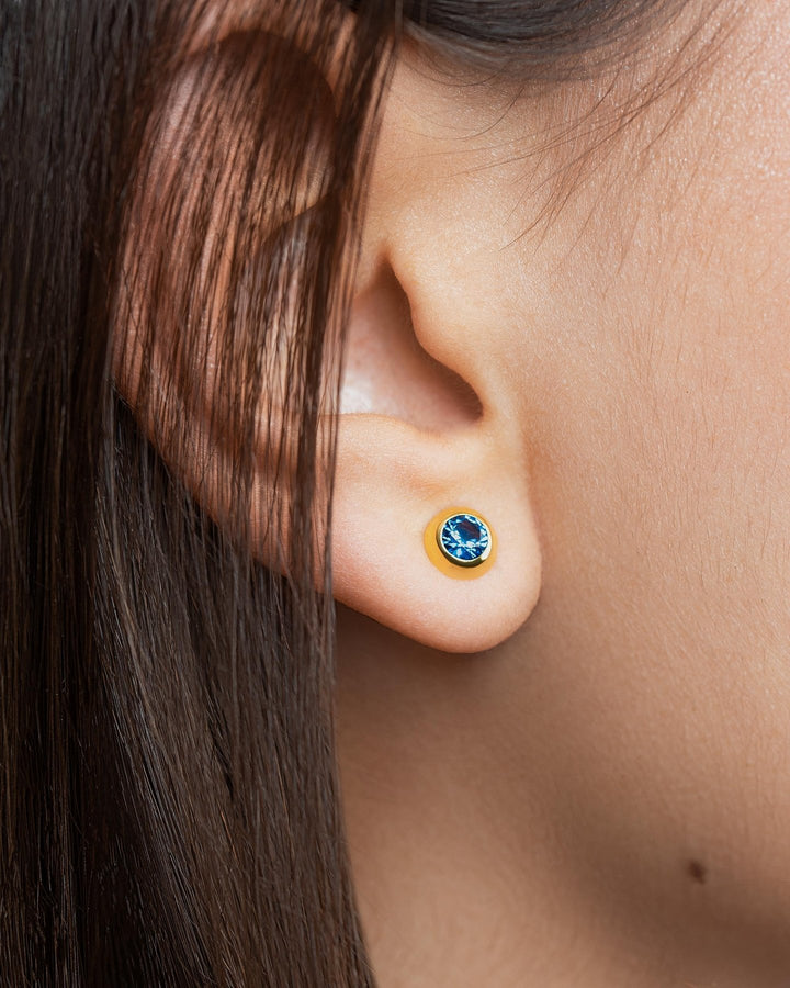 Close-up of blue stone earring on ear – detailed view of a woman wearing a gold and blue gemstone stud earring.