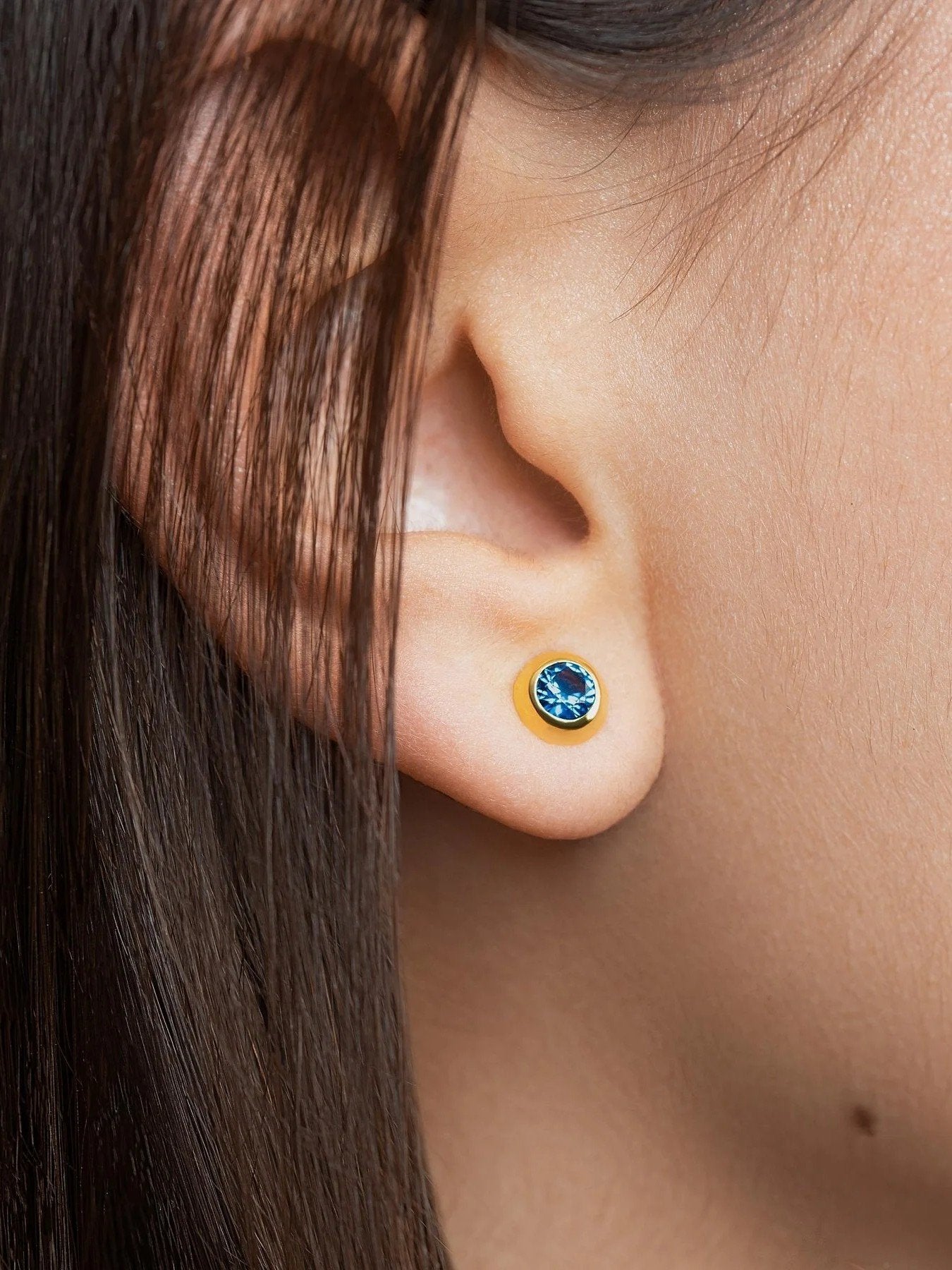 Close-up of blue stone earring on ear – detailed view of a woman wearing a gold and blue gemstone stud earring.