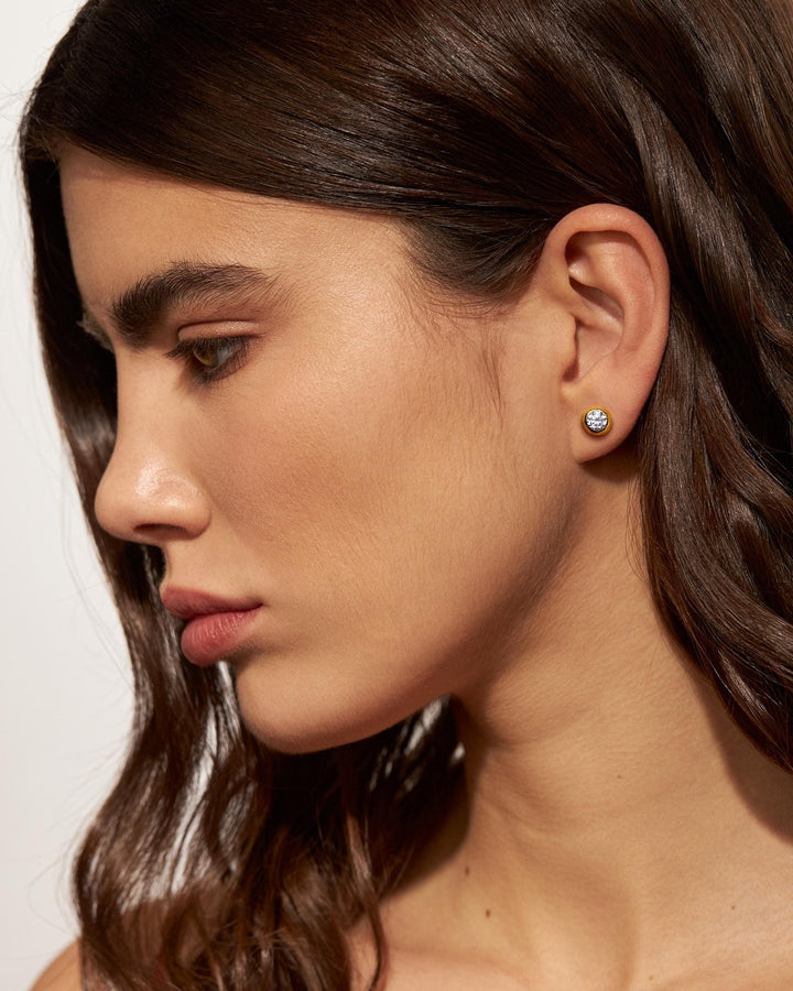 Woman wearing gold earrings with a white stone – model with loose hair showcasing gold and gemstone earrings.