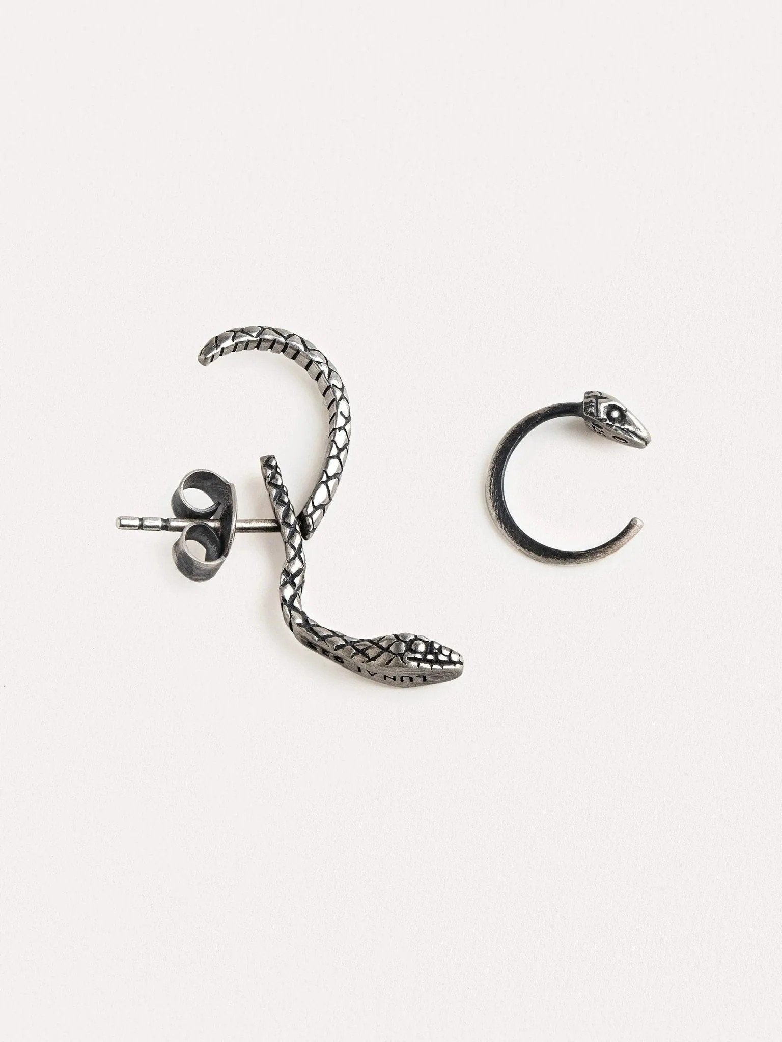 Close-up of an oxidized silver snake hoop earring on an ear, highlighting its textured details and unique shape.