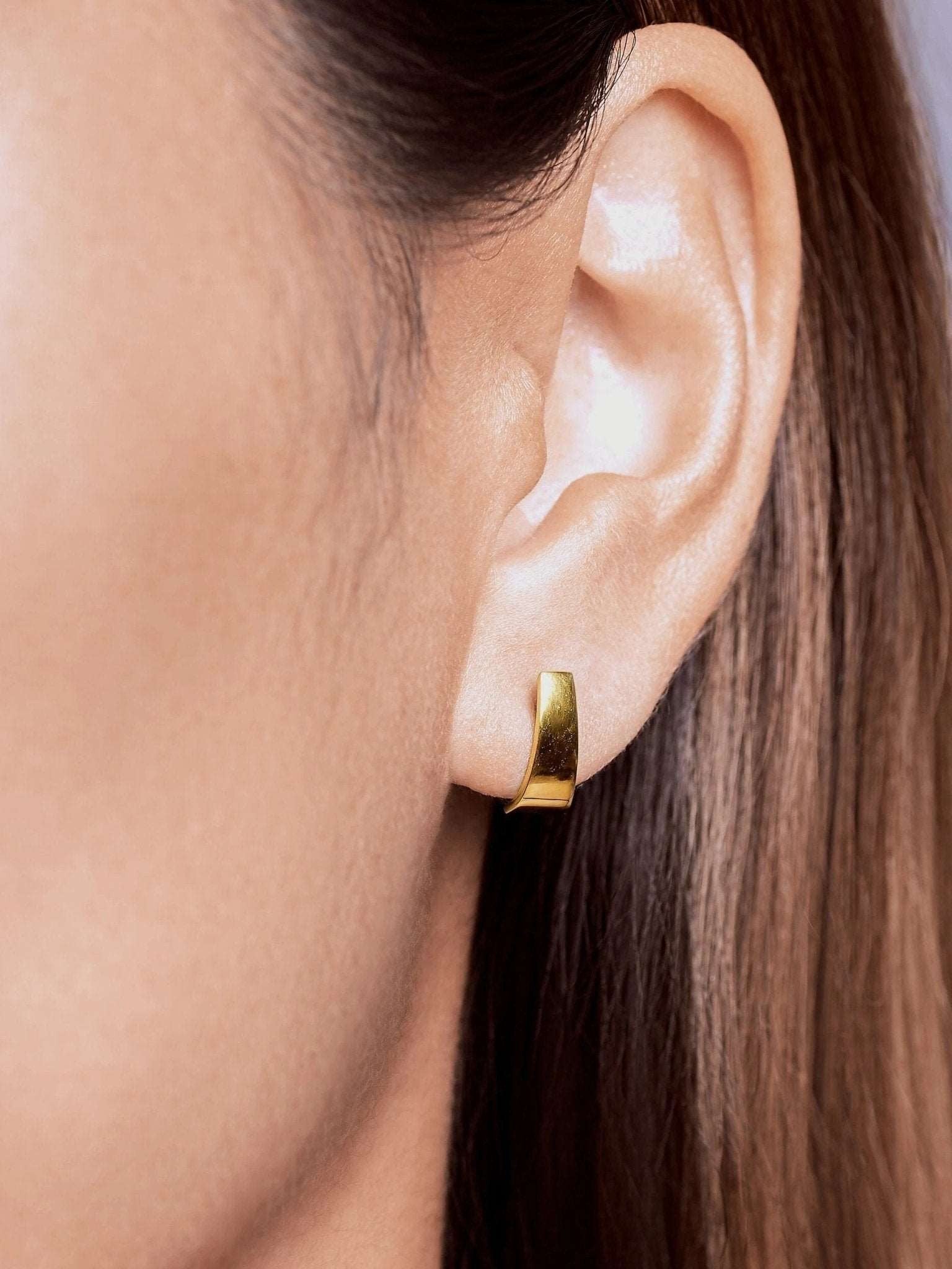 Terita gold stud earring worn — soft, polished curve styled on ear.