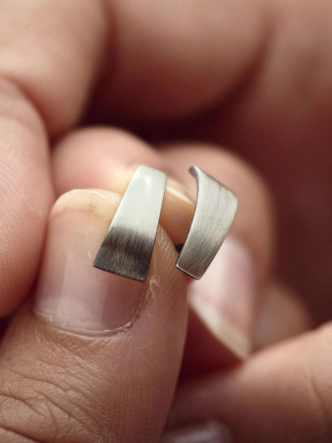 Close-up of Terita stud earring in oxidized silver held in hand — matte surface and curved minimalist design.
