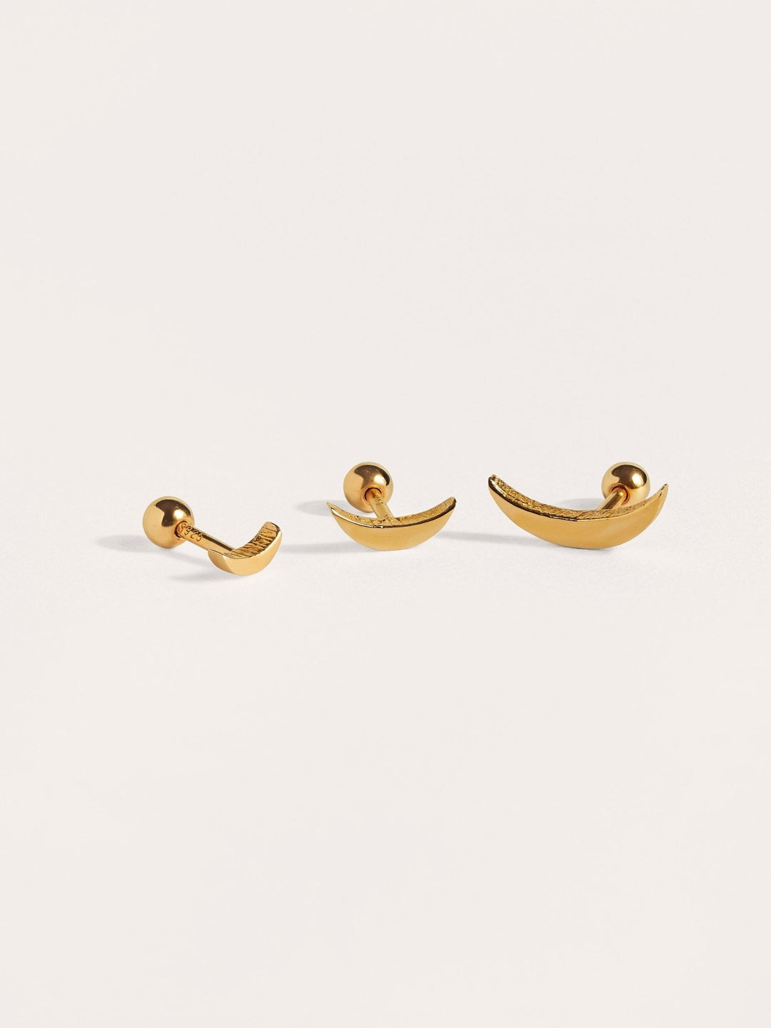 Minimalist gold cartilage piercings laid flat, showing curved shape and handcrafted finish.