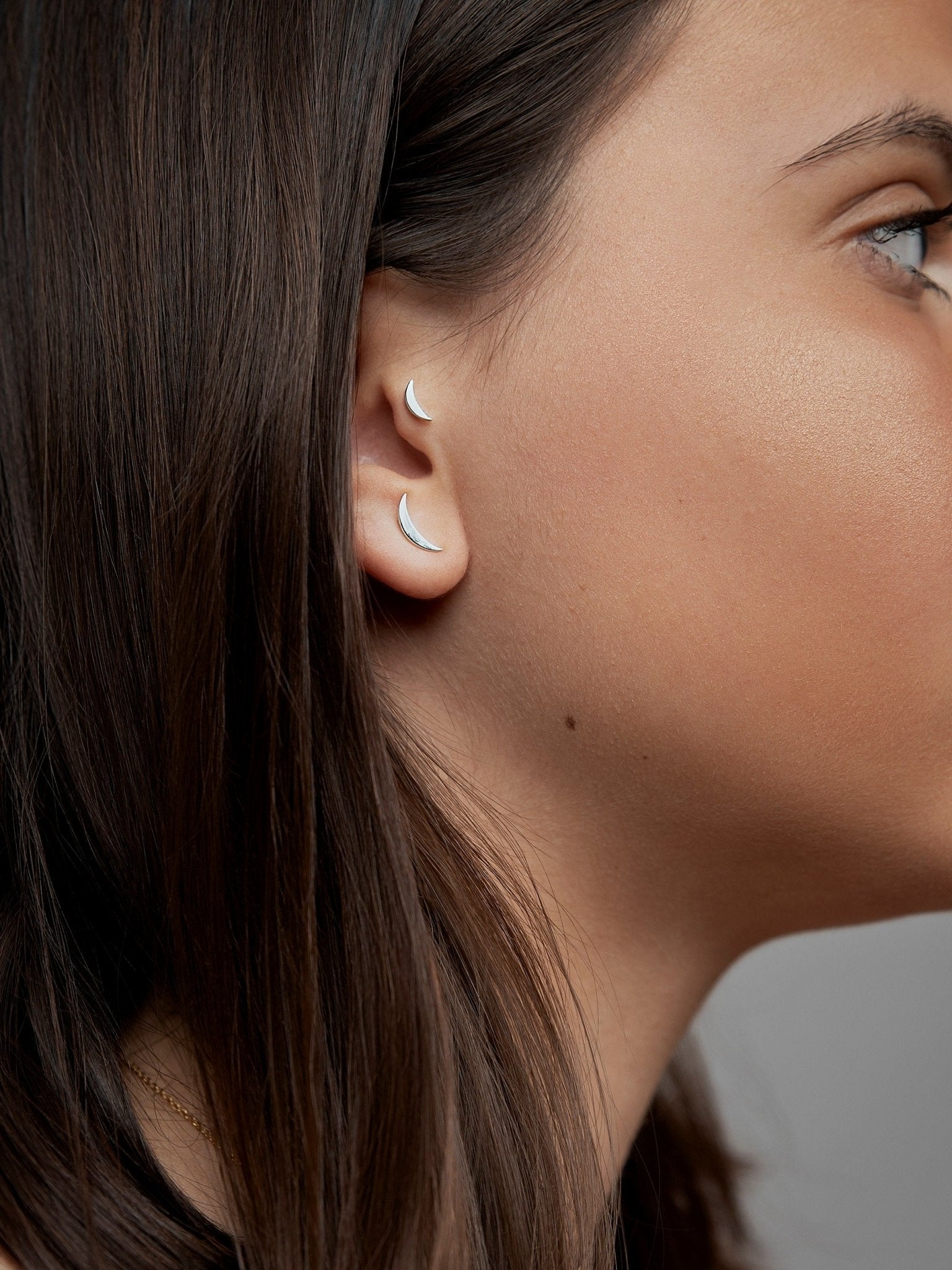 Profile view of woman wearing the Athina piercing, highlighting the gold detail on her ear.