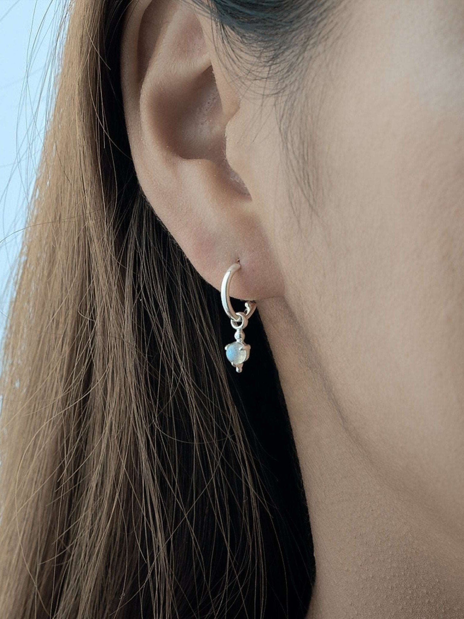 Model wearing gold hoop earrings with moonstone charm, left side view