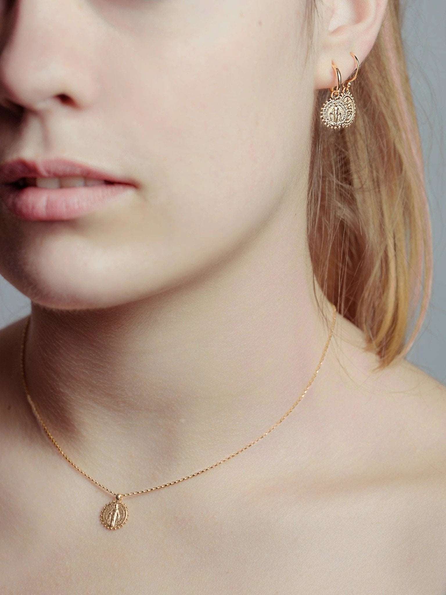 Side view of gold plated Codi Mini Hoops – Virgin Mary charm gently resting near the neck.