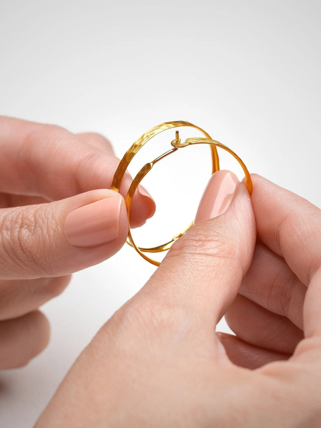 Hand holding a pair of hammered 24K gold matte hoop earrings – showing top and bottom details, handmade and sustainable.