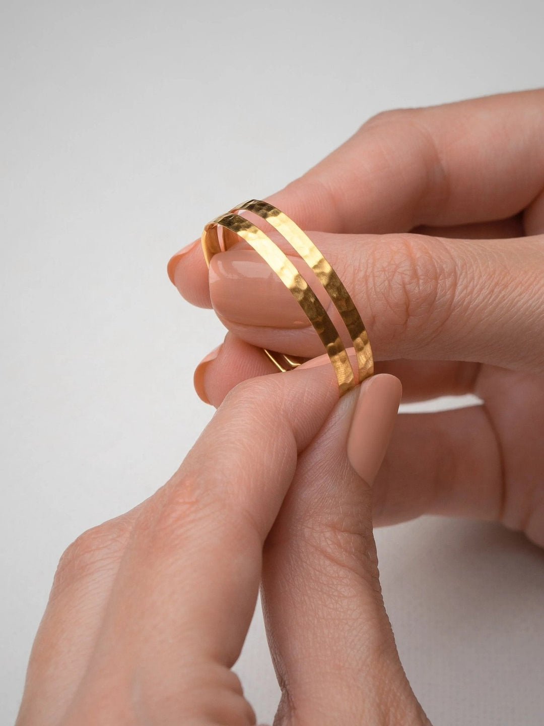 Hands holding a pair of hammered 24K gold matte hoop earrings – showcasing both earrings, handmade and sustainable.