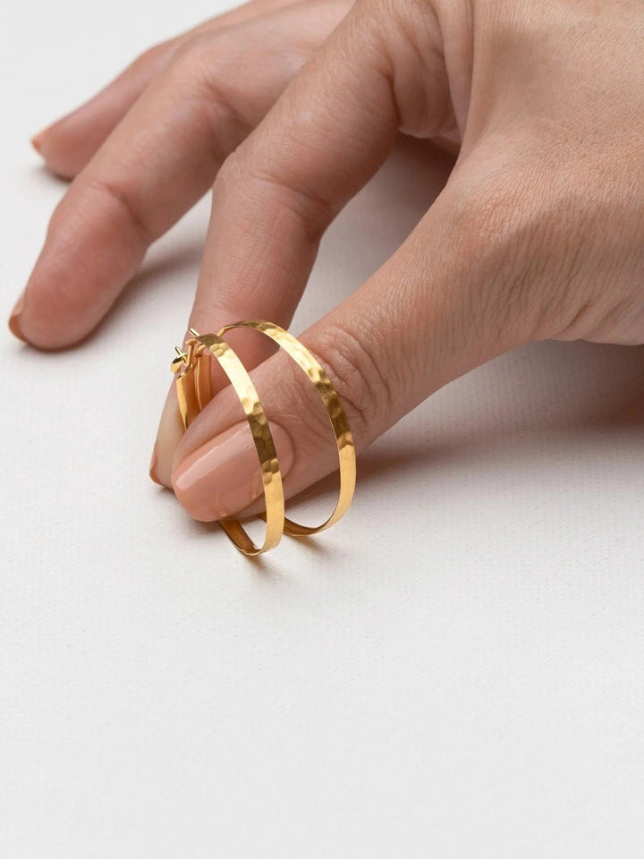 Hand holding 24K gold-plated matte hammered hoop earring – handmade and eco-friendly.