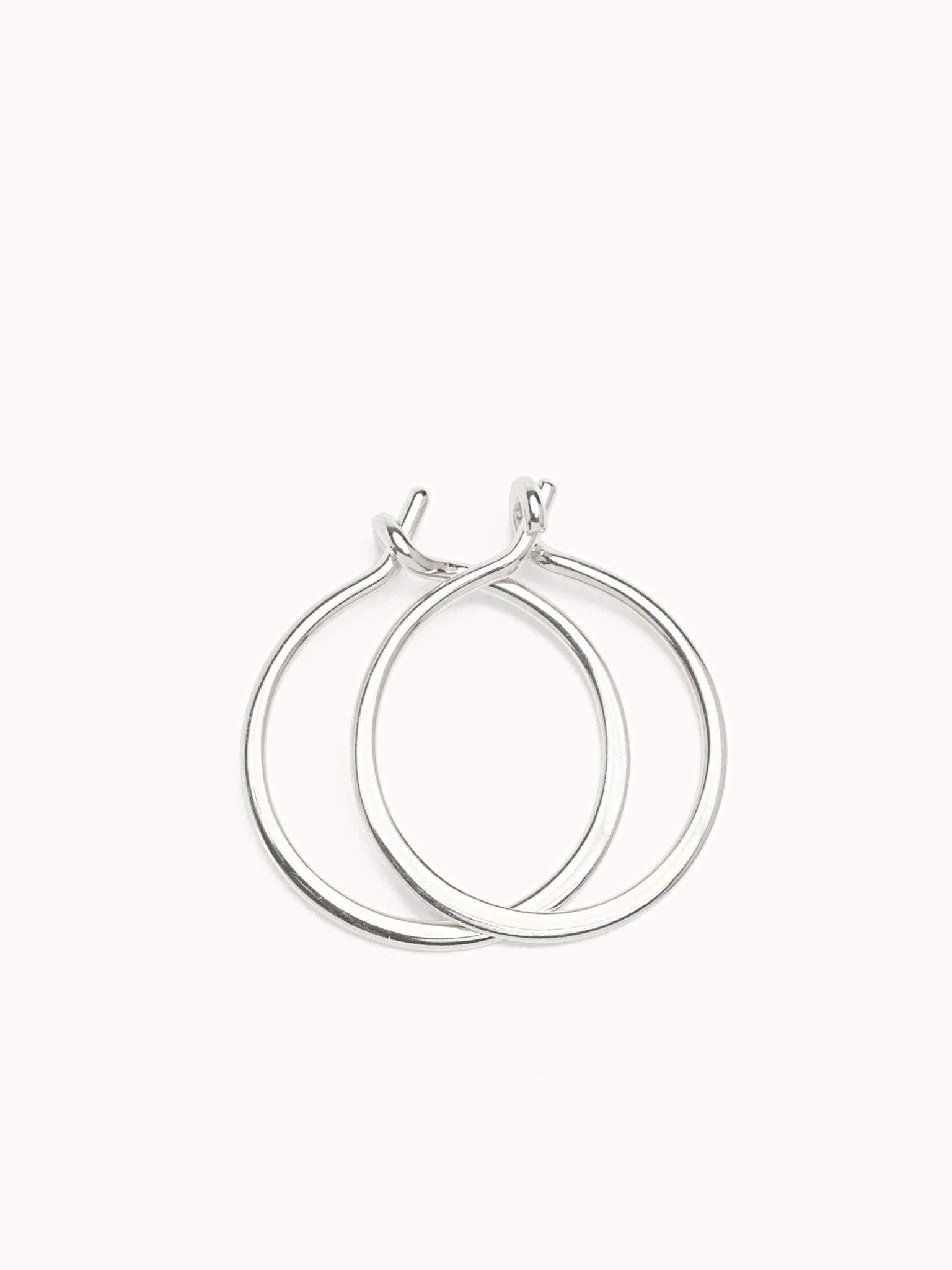 Double sterling silver hoop earrings with an intertwined modern design on a soft pink background