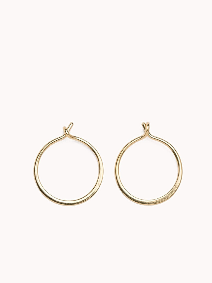 Minimalist 14K gold filled hoop earrings with a small open closure on a soft pink background