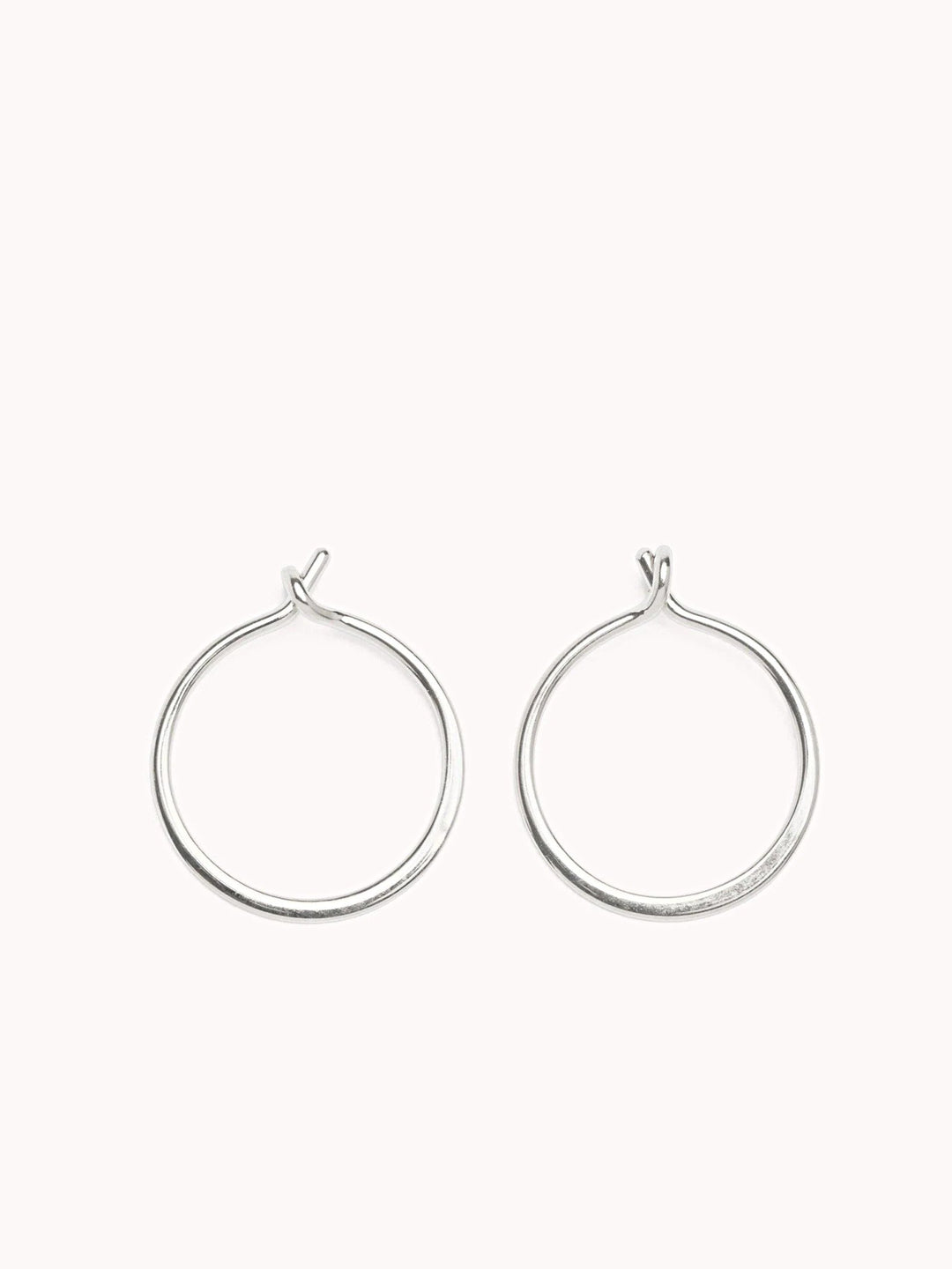 Sterling silver minimalist hoop earrings with an open closure on a soft pink background
