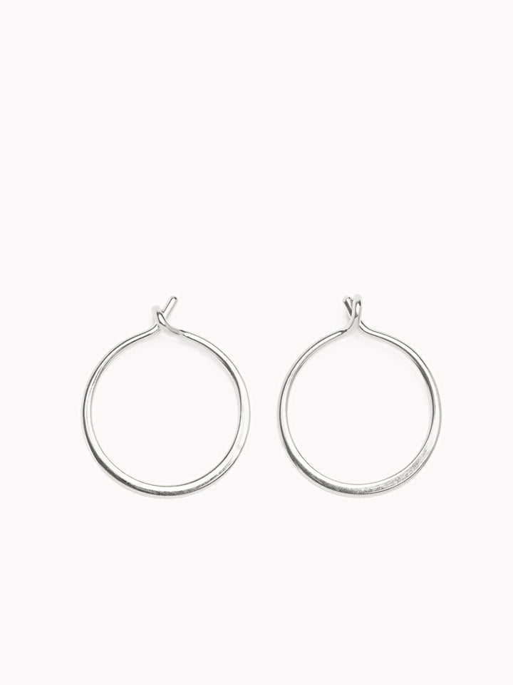 Sterling silver minimalist hoop earrings with an open closure on a soft pink background