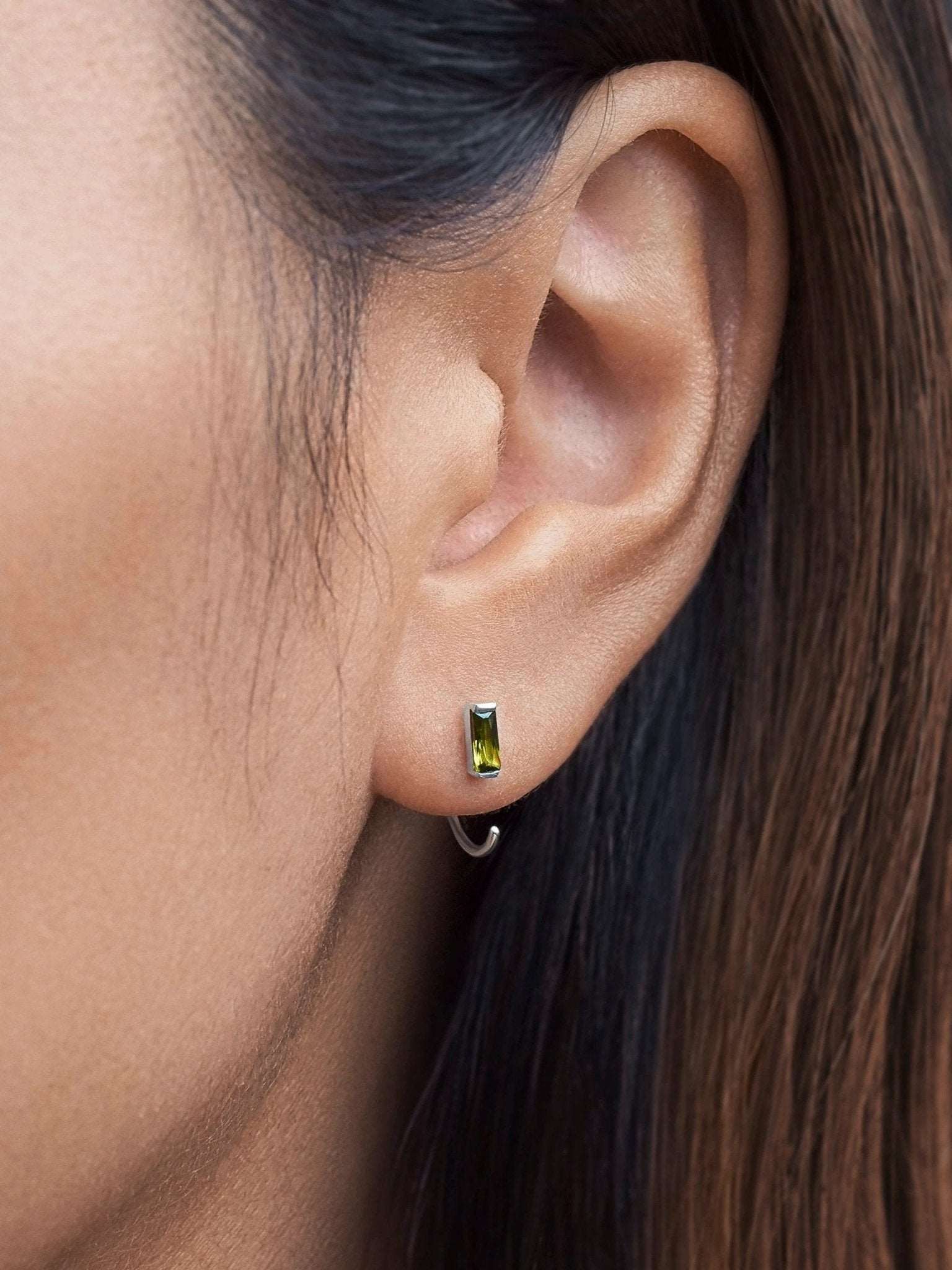 Woman wearing peridot open hoop earrings in rose gold, showcasing their elegant and minimalist design.