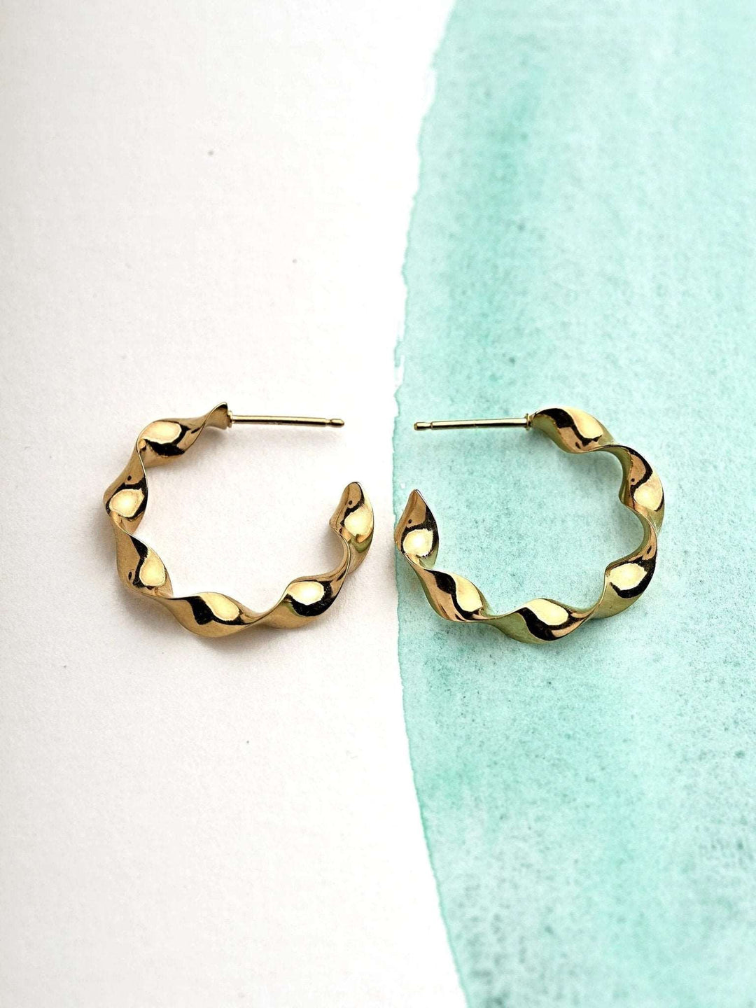 "Gene Twisted Hoop Earrings in gold on neutral background"