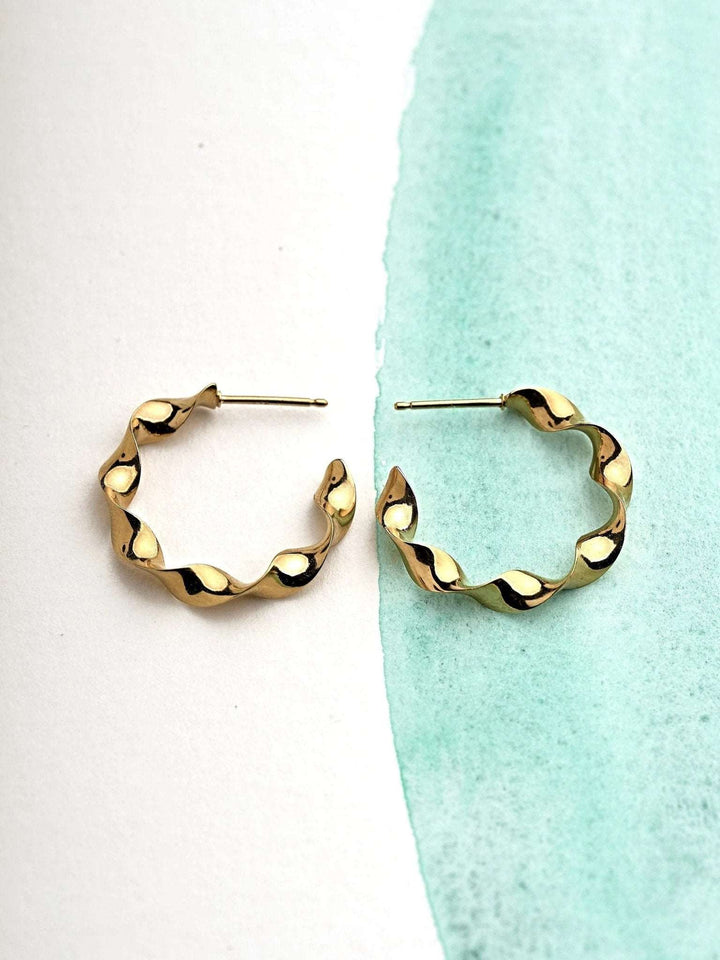 "Gene Twisted Hoop Earrings in gold on neutral background"