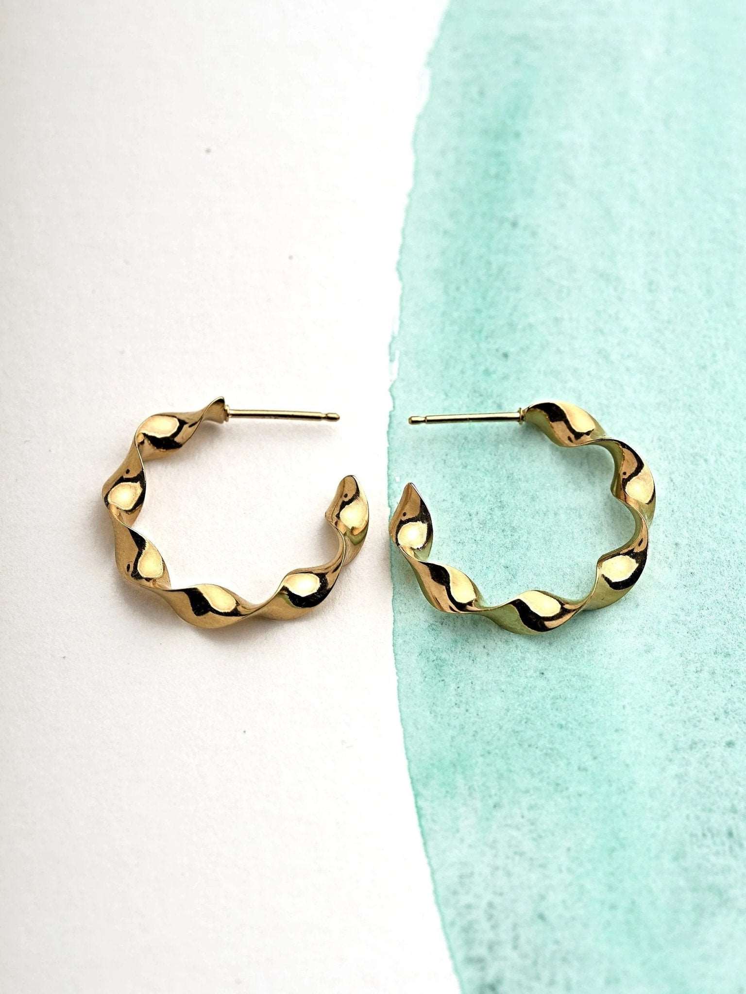 "Gene Twisted Hoop Earrings in gold on neutral background"
